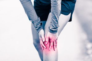 Runners knee leg pain, woman holding sore and overtrained painful knee, sprain or cramp ache filled with red pink bright place. Overtraining injured person when exercising or running outdoors.